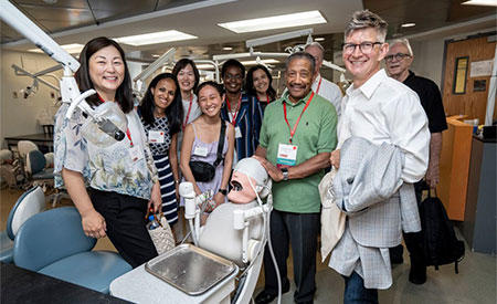 A group of alumni standing around an operatory chair.