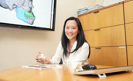 Dr. Janice Lee sitting at her desk holding a model of a set of teeth.