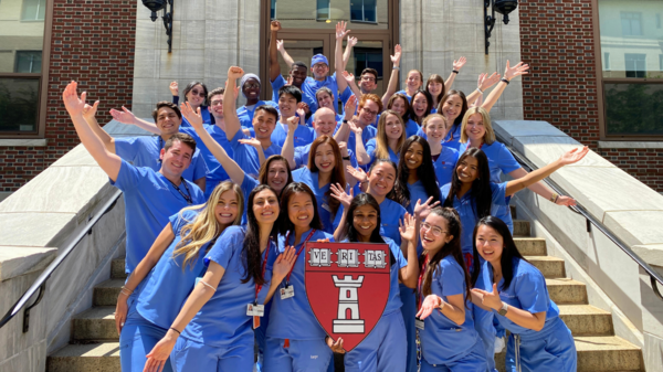 dental students in light blue scrubs stand on the front steps of hsdm smiling and celebrating