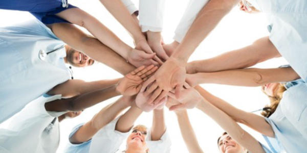 An upward view of a circle of people placing their hands on top of each other in a sign of unity.