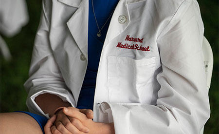 student in her white coat showing the Harvard Medical School embroidered  on it.