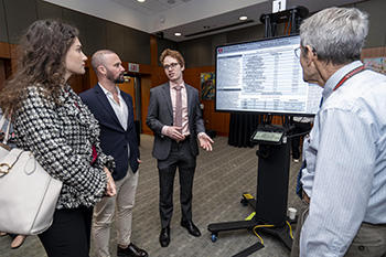 Student presenting his research on a computer screen to two faculty members.