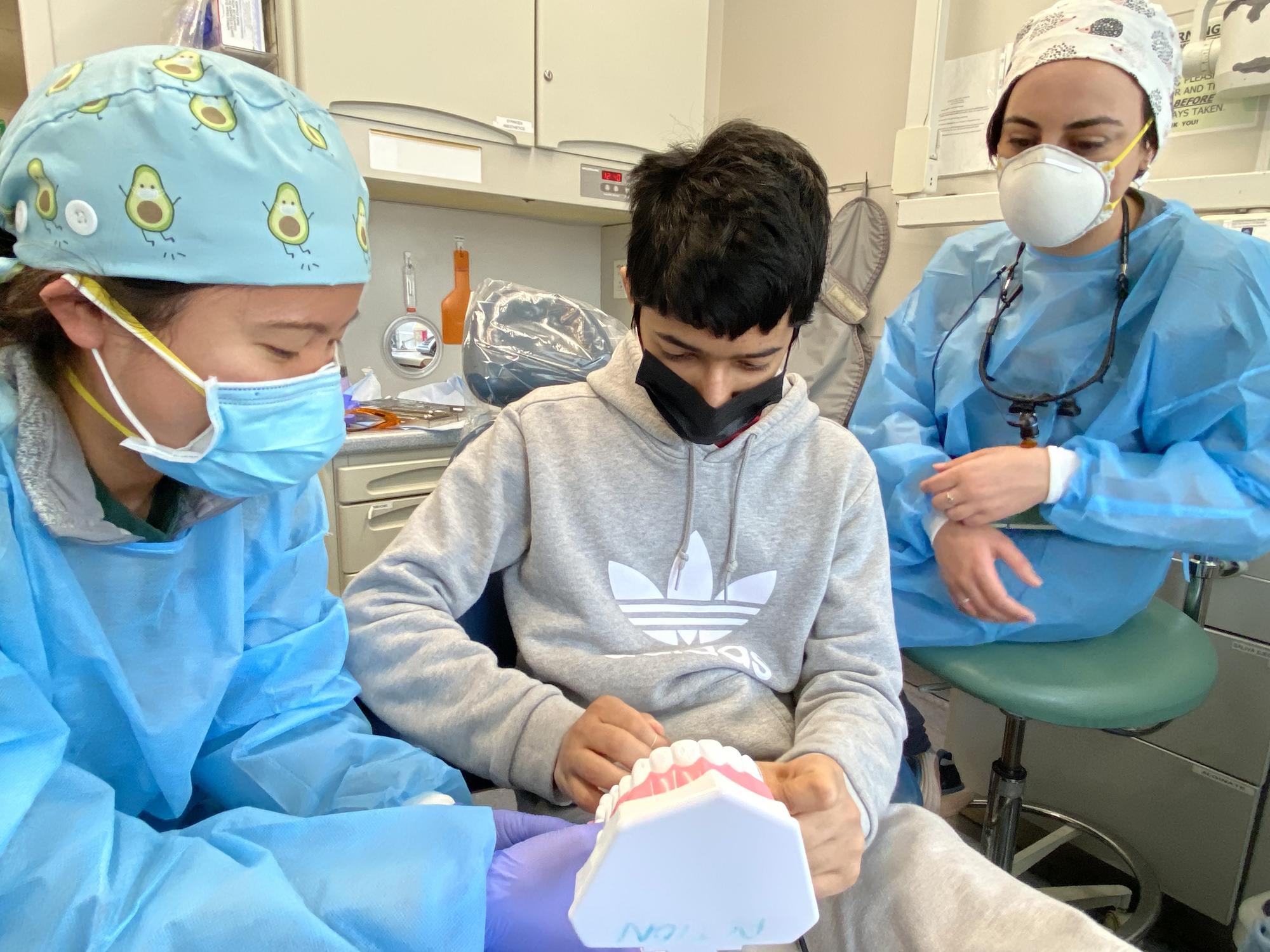 Two dentists showing young patient how to properly brush their teeth