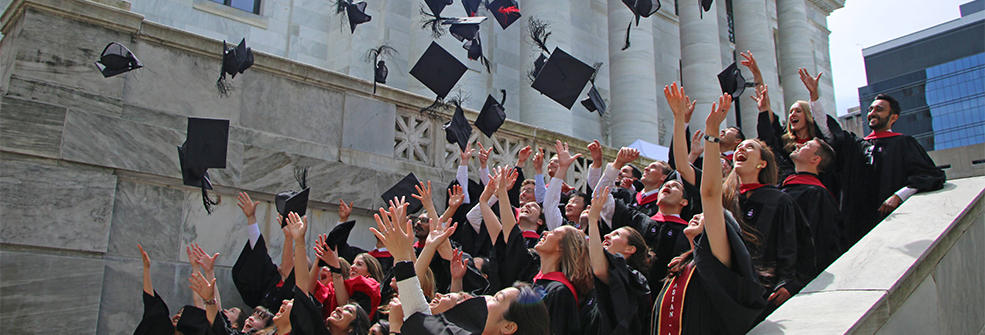 Students on the steps of HMS's Gordon Hall tossing their graduation caps in the air.