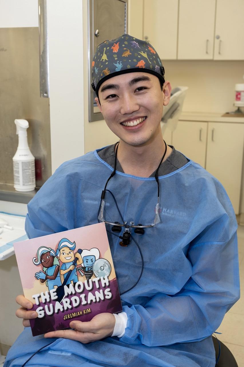 Student wearing scrubs holding book "The Mouth Guardians"