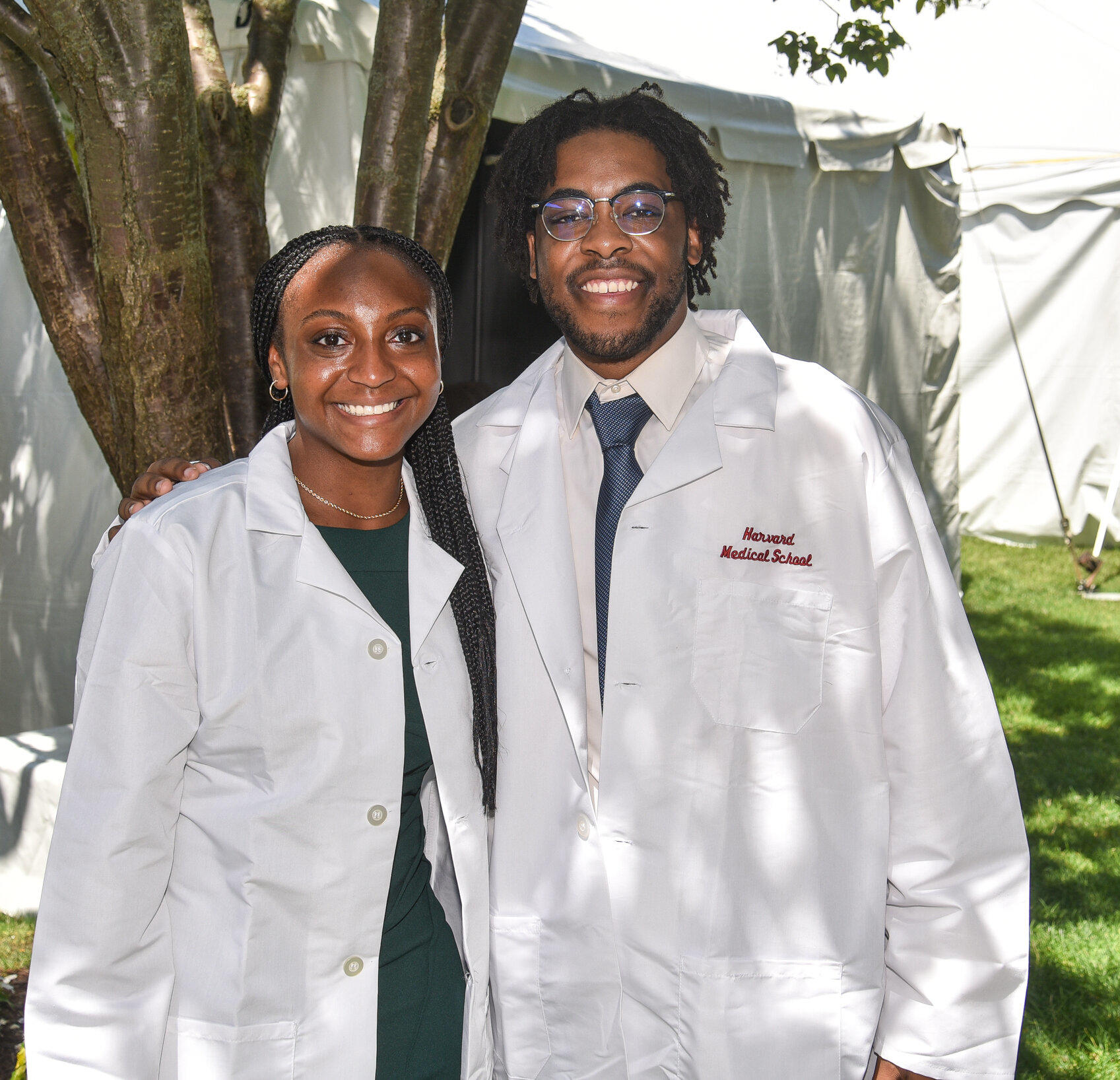 Two students standing together outside wearing HMS white coats