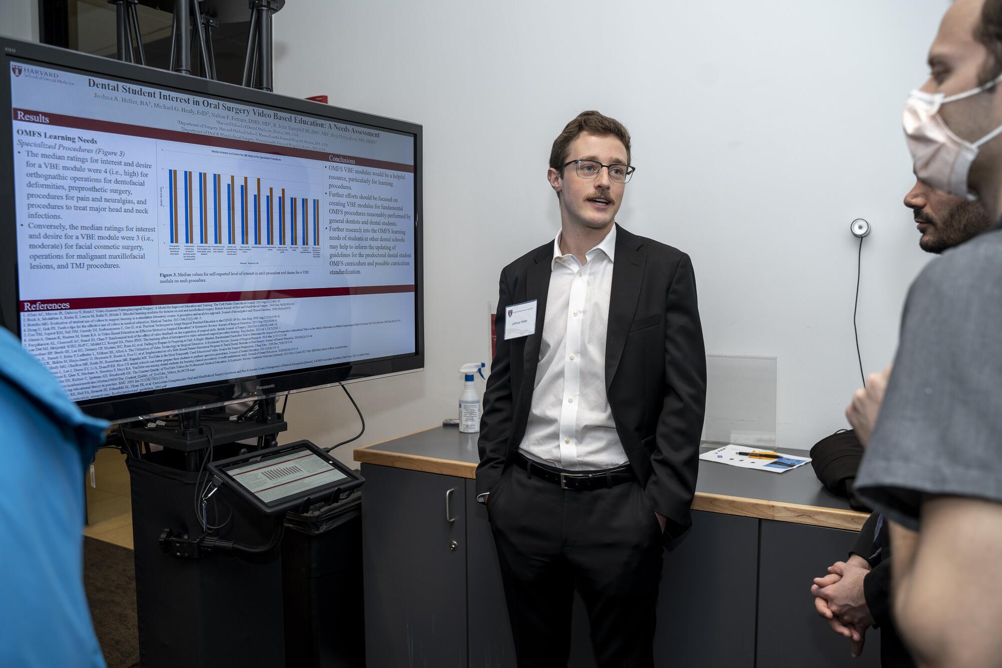 Male student, standing by digital screen, presenting research project to peers