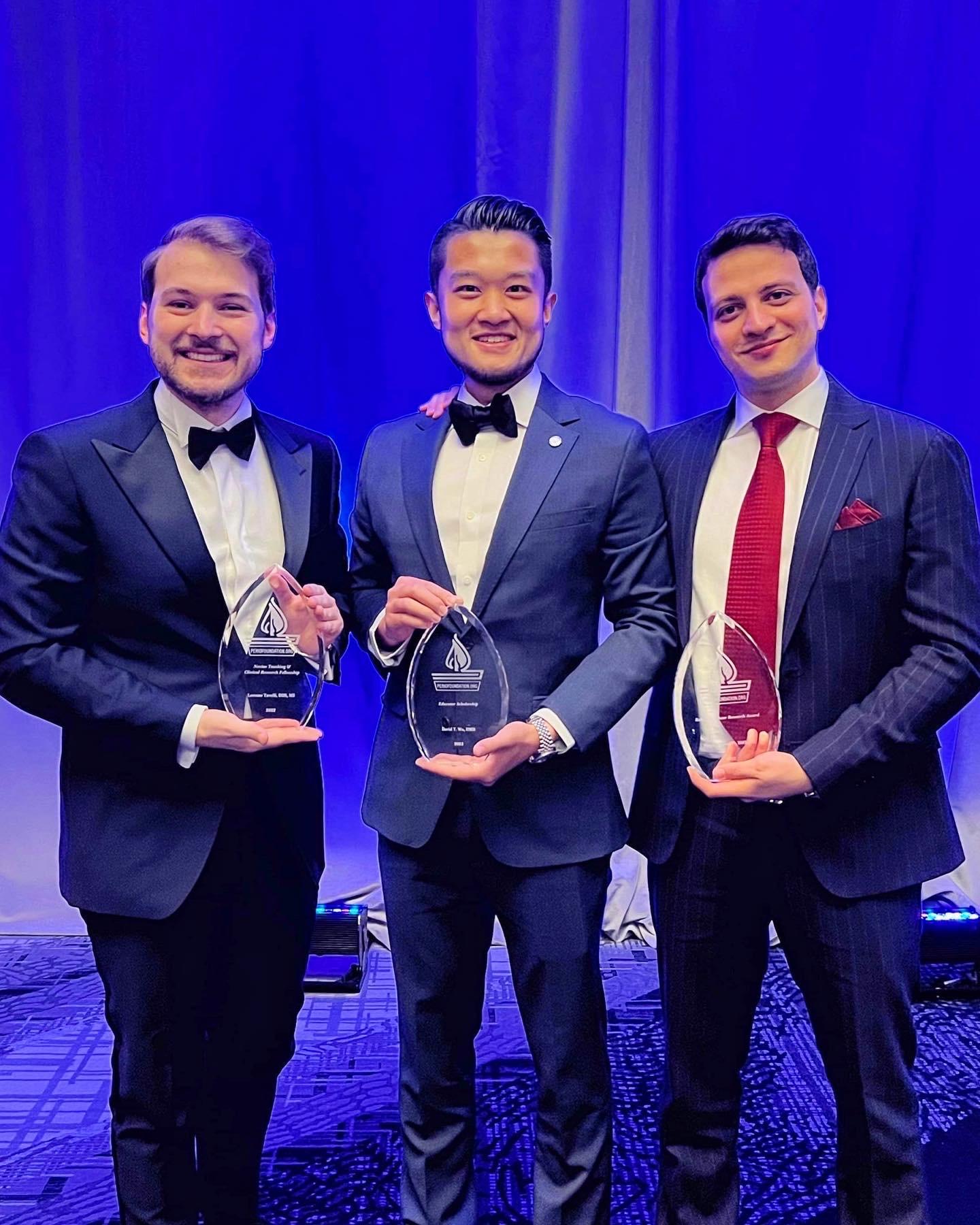 Three people dressed in suits holding glass awards