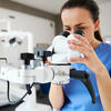 woman in blue scrubs looks into dental microscope