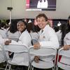 Four students wearing white coats sitting in ceremony