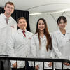 four students face the camera all smiling and donning their white coats,